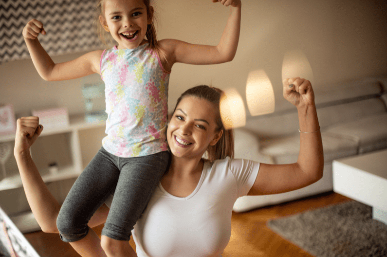 smiling young girl showing strong arms sat on shoulder of smiling mum